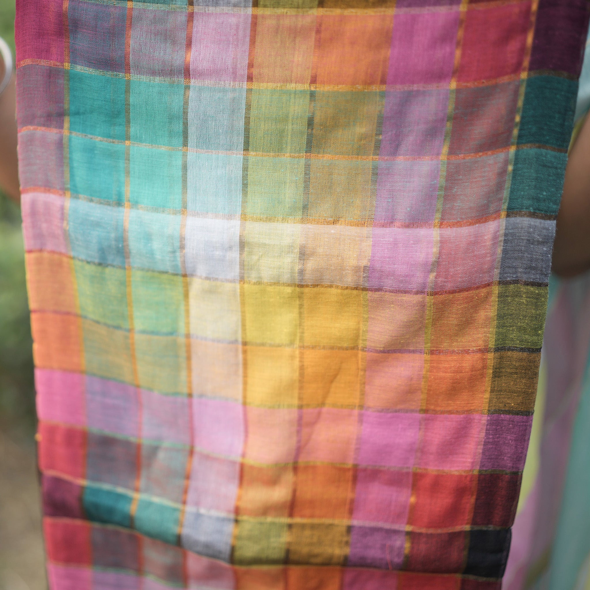 Multicolored checkered fabric held by a person with a blurred natural background