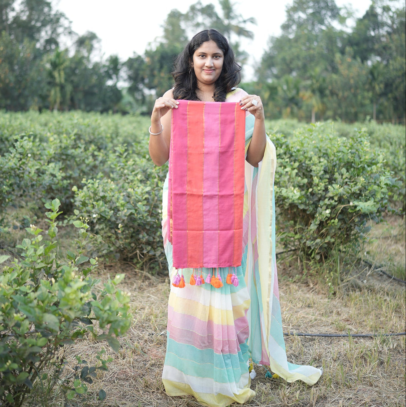 Woman holding a colorful striped fabric in an outdoor setting with greenery.